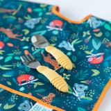 Close-up of Bumkins Spoon + Fork: Pineapple on top of a dark blue animal-themed bib on a white background.
