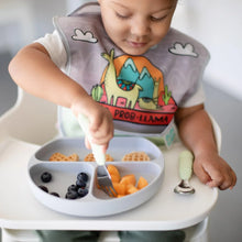 Load image into Gallery viewer, A toddler wearing a llama bib in a high chair uses Bumkins Spoon + Fork: Sage to eat fruit and waffles from a gray sectioned plate.
