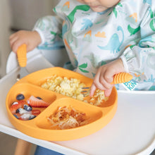 Load image into Gallery viewer, A child uses Bumkins Spoon + Fork: Tangerine to eat eggs and fruit from an orange sectioned plate while wearing a dinosaur-print bib.

