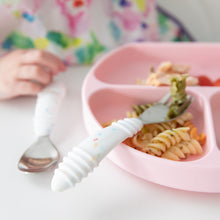 Load image into Gallery viewer, Close-up of a child's hand near a pink plate with pasta and veggies, and Bumkins Spoon + Fork: Vanilla Sprinkle on a white table.
