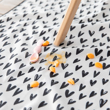 Load image into Gallery viewer, Close-up of a spoon and squashed orange pieces on a Bumkins Splat Mat: Hearts underneath a high chair.
