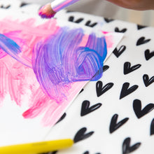 Load image into Gallery viewer, Close-up of a child painting with pink and purple on white paper over a Bumkins Splat Mat: Hearts.
