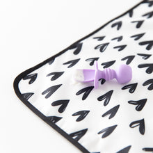 Load image into Gallery viewer, Close-up of a purple baby spoon with food sitting on a Bumkins Splat Mat: Hearts, made from easy-wipe fabric, on a white background.
