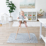 A baby in a high chair with a bib sits on a Bumkins Splat Mat: Charcoal Check, surrounded by bright modern decor.