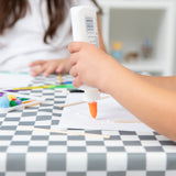 A child crafts with glue and other colorful art supplies on a Bumkins Splat Mat: Charcoal Check.