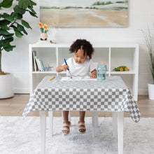 Load image into Gallery viewer, A child paints with watercolors at a table covered in a Bumkins Splat Mat: Charcoal Check, surrounded by toys and a plant.
