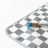 Close-up of a paintbrush with blue paint resting on a Bumkins Splat Mat: Charcoal Check on a white background.