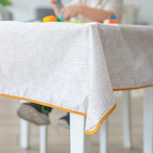 Load image into Gallery viewer, Close-up of a Bumkins Splat Mat: Wander draped over a table, with a child blurred in the background.
