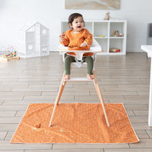 Load image into Gallery viewer, A toddler in a high chair wearing an orange bib sits on top of a Bumkins Splat Mat: Grounded covered in food.
