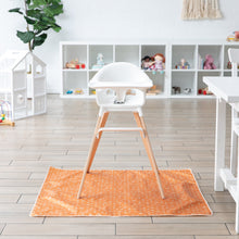 Load image into Gallery viewer, A white high chair sits on Bumkins Splat Mat: Grounded in a playroom, with toy-filled shelves in the background.
