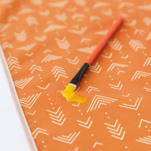 Load image into Gallery viewer, Close-up of a paintbrush with yellow paint resting on a Bumkins Splat Mat: Grounded on a white background.
