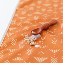 Load image into Gallery viewer, Close-up of small cereal pieces and spilled milk next to a brown spoon on Bumkins Splat Mat: Grounded on a white background.
