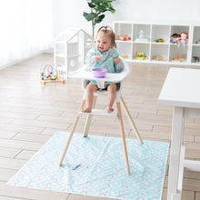 Load image into Gallery viewer, A toddler eats from a purple bowl in a high chair while Bumkins Splat Mat: Rainbows covers the floor below; a purple spoon sits on top.
