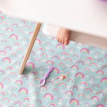 Load image into Gallery viewer, A baby's foot peeks from under a high chair tray, while Bumkins Splat Mat: Rainbows lays below with a purple spoon and yogurt smear on top.
