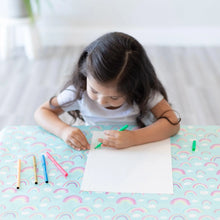 Load image into Gallery viewer, A girl draws on white paper with colored pens at a table covered by a Bumkins Splat Mat: Rainbows.
