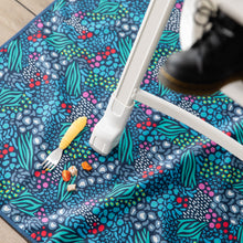 Load image into Gallery viewer, Bumkins Splat Mat: Animal Prints lays under a high chair, with a yellow fork and pieces of food on top.
