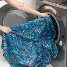 Load image into Gallery viewer, A person places a Bumkins Splat Mat: Animal Prints into an open front-load washer for easy cleaning.
