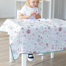 Load image into Gallery viewer, A child in a white shirt crafts at a table covered by a Bumkins Splat Mat: Floral in a bright room.
