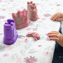 Load image into Gallery viewer, Close-up of a child playing with a purple sandcastle mold and kinetic sand on a Bumkins Splat Mat: Floral.
