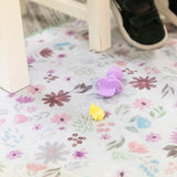 Bumkins Splat Mat: Floral lays on a floor under a chair, with a purple baby spoon and yellow food on top.