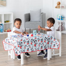 Load image into Gallery viewer, Two kids joyfully paint at a small table covered with Bumkins Splat Mat: Mickey Mouse in a bright playroom.
