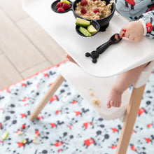 Load image into Gallery viewer, A child in high chair eats oatmeal, berries, and avocado from a bowl with a spoon; Bumkins Splat Mat: Mickey Mouse covers the floor below.

