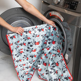 A person places Bumkins Splat Mat: Mickey Mouse into an open front-loading washing machine.