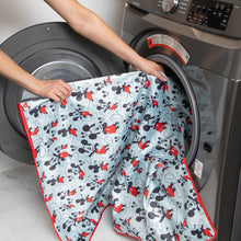 Load image into Gallery viewer, A person places Bumkins Splat Mat: Mickey Mouse into an open front-loading washing machine.
