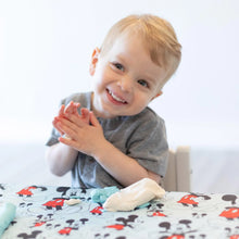 Load image into Gallery viewer, A toddler in grey shirt smiles and claps hands at a table covered by Bumkins Splat Mat: Mickey Mouse.
