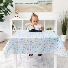 Load image into Gallery viewer, A toddler snacks from a black tray atop a Bumkins Splat Mat: Mickey + Minnie Sunny Side Up on a table, white shelves and a plant behind.
