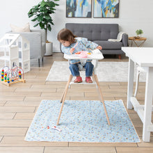 Load image into Gallery viewer, A toddler eats in a high chair on a Bumkins Splat Mat: Mickey + Minnie Sunny Side Up, surrounded by a gray sofa and playhouse.
