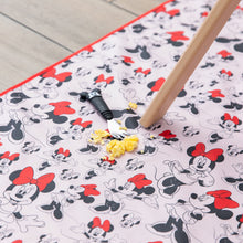 Load image into Gallery viewer, Scrambled eggs and a Mickey Mouse fork sit on a Bumkins Splat Mat: Minnie Mouse, under a wooden table leg on the floor. 
