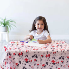 Load image into Gallery viewer, A child draws with markers on a table covered by Bumkins Splat Mat: Minnie Mouse with a potted plant in the background.
