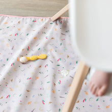 Load image into Gallery viewer, A yellow spoon with yogurt sits on top of Bumkins Splat Mat: Princess Magic underneath a high chair with a baby's foot visible.
