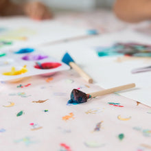 Load image into Gallery viewer, Close-up of colorful paint blobs, a blue-covered brush, and paper on a table covered by Bumkins Splat Mat: Princess Magic.
