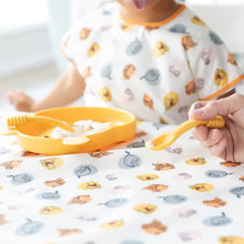 Load image into Gallery viewer, A child sits at table with a Bumkins Splat Mat: Winnie and Friends, with a dish of yogurt in front of them. An adult holds a spoon nearby.
