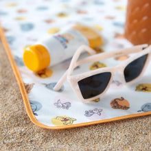 Load image into Gallery viewer, Close-up of sunglasses and sunscreen resting on a Bumkins Splat Mat: Winnie and Friends on sand.
