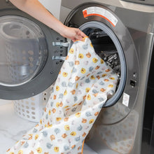 Load image into Gallery viewer, A person places Bumkins Splat Mat: Winnie and Friends in an open front-loading washing machine.
