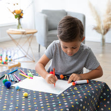 Load image into Gallery viewer, A young boy draws at a table covered by a Bumkins Splat Mat: Super Mario™ Lineup in a bright living room.
