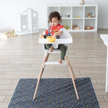 Load image into Gallery viewer, A girl eating from a yellow bowl sits in a high chair on top of a Bumkins Splat Mat: Super Mario™ Lineup in a brightly lit playroom.
