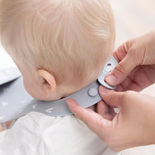 Load image into Gallery viewer, Adult hands fasten the closure of a Bumkins Silicone Bib: Hearts around a baby's neck over a white shirt.
