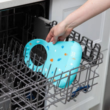 Load image into Gallery viewer, A person places Bumkins Silicone Bib: Ocean Life into the top rack of an open dishwasher.

