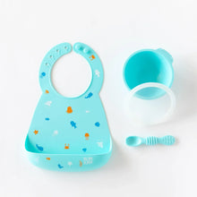 Load image into Gallery viewer, Bumkins Silicone Bib: Ocean Life lays next to a blue bowl &amp; spoon set on a white background.
