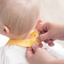Load image into Gallery viewer, Hands fasten the closure of a Bumkins Silicone Bib: Camp Gear around a baby's neck.

