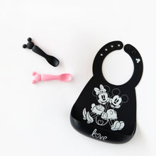 Load image into Gallery viewer, Bumkins Silicone Dipping Spoons: Minnie Mouse (Black and Pink) lay next to a black bib with a Mickey &amp; Minnie design on a white background.
