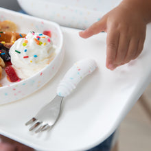 Load image into Gallery viewer, Close-up of a child's hand reaching for a Bumkins Spoon + Fork: Vanilla Sprinkle next to a matching plate with waffles on a high chair tray.
