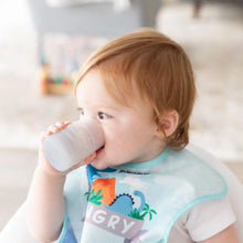 Load image into Gallery viewer, A toddler with red hair drinks from a Bumkins Silicone Starter Cup: Gray while wearing a dinosaur-themed bib.
