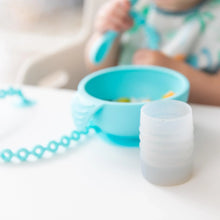 Load image into Gallery viewer, Bumkins Silicone Starter Cup: Gray sits on a white table next to a blue bowl, with a child holding a blue spoon blurred in the background.
