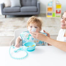 Load image into Gallery viewer, A woman helps a baby in a dinosaur bib drink from a Bumkins Silicone Starter Cup: Gray at a white table with a bowl and spoon.
