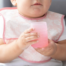 Load image into Gallery viewer, Close-up of a baby in a pink patterned bib holding a Bumkins Silicone Starter Cup: Pink.
